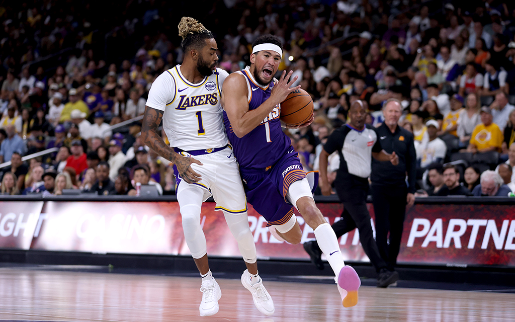 Devin Booker and D’Angelo Russell in action on the court with a crowd and referees in the background.