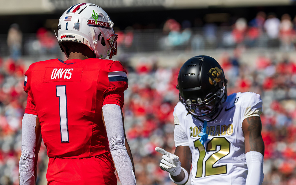 Two football players on a field, one in a red uniform with "Davis" and "1," the other in white with "12," pointing.