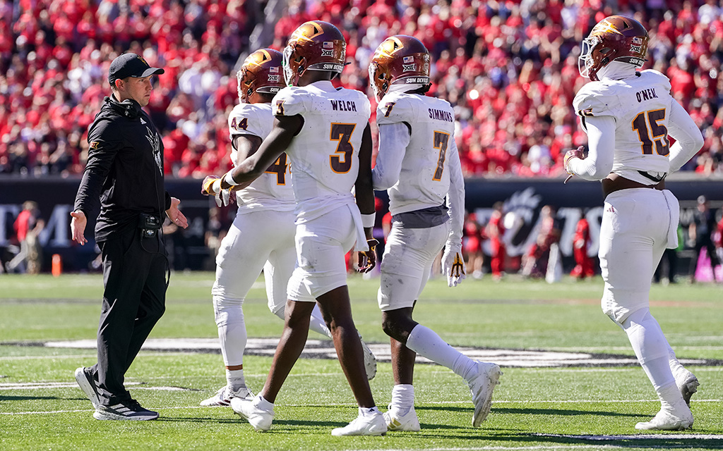 American football players in white jerseys walking towards a coach on the field.