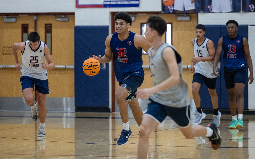 A basketball player in a blue jersey with the number 32 dribbles a basketball on an indoor court.