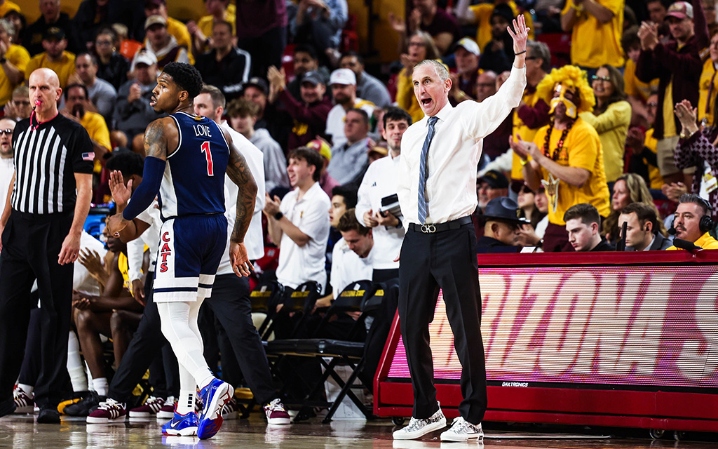 Arizona guard Caleb Love and Arizona State head coach Bobby Hurley during a game, surrounded by a lively audience.
