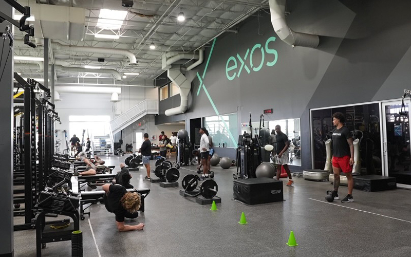People working out in a spacious gym with "exos" logo on the wall.