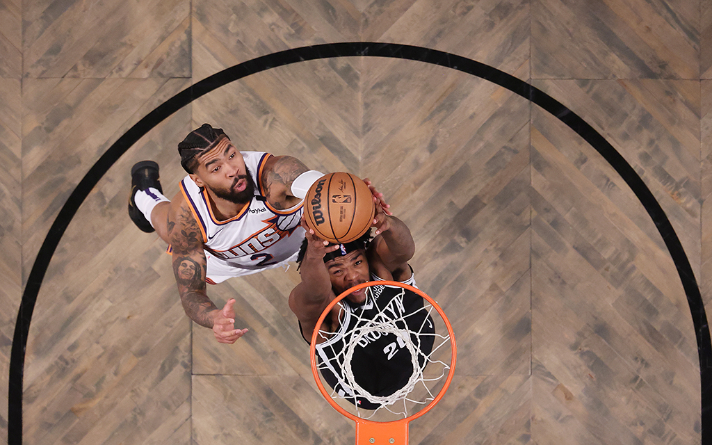 Overhead view of Phoenix Suns center Nick Richard and Brooklyn Nets player near a hoop with a wooden court background.