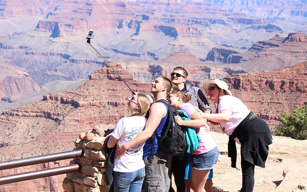 A group of five people taking a selfie with the Grand Canyon in the background.