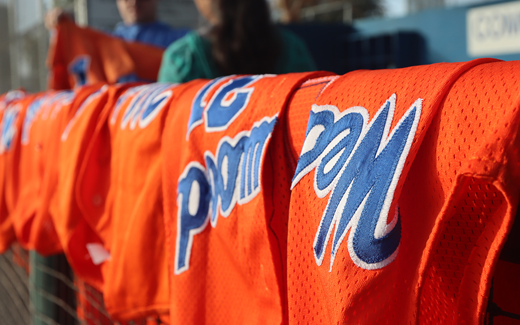 Orange Westwood High School baseball jerseys with blue lettering hanging over a fence.