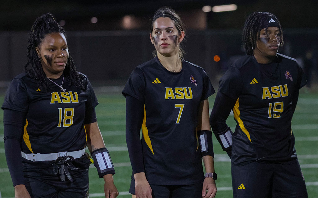 ASU flag football co-founder Sophia Smith, quarterback Allison Rodriguez and co-founder Sierra Smith with numbers 18, 7, and 19 stand on a sports field.