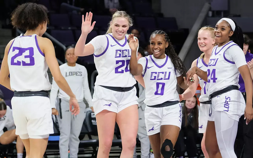 Five GCU women's basketball players in white and purple uniforms celebrating on a court.