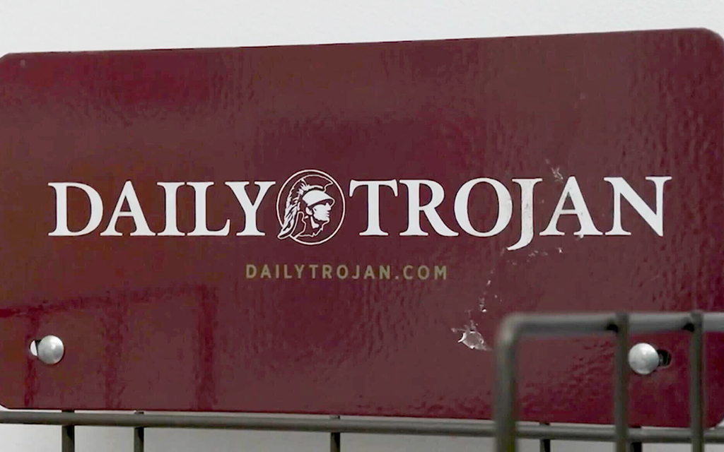 Maroon sign with "DAILY TROJAN" and a Roman helmet emblem.