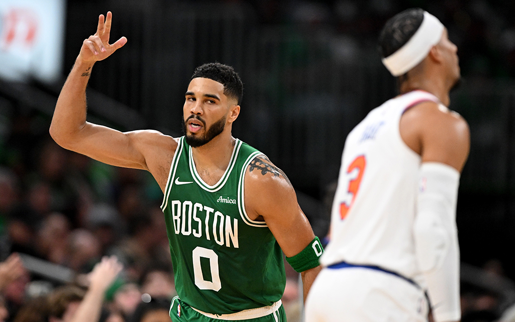 Jayson Tatum in a green Boston jersey raises three fingers during a game.