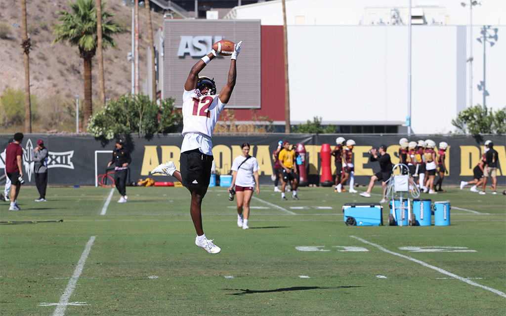 A football player wearing jersey number 12 jumps to catch a ball during practice on field.