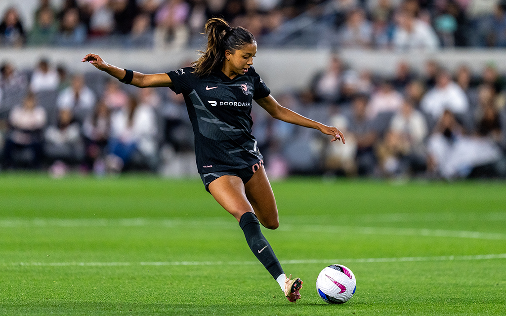 Madison Hammond prepares to kick a ball on a grassy field with spectators in the background.