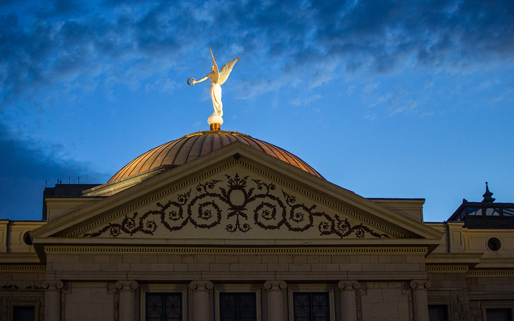 Arizona State Capitol with a copper dome and a winged statue, set against a blue evening sky.