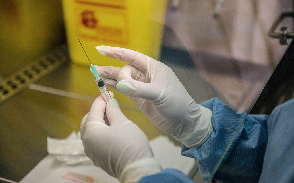 Gloved hands handling a needle for a vaccine.